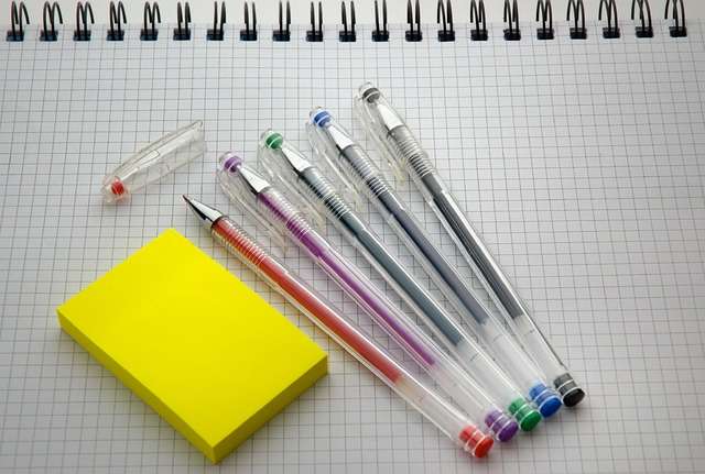 Kleurige pennen en een gele notitieblok op een geruit notitieboek, symboliserend voorbereiding voor ISO 9001, ISO 14001 en ISO 27001 auditortrainingen.