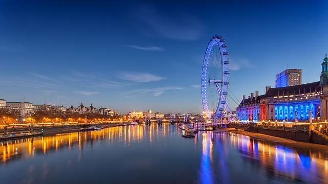 Londense skyline met de London Eye en verlichte gebouwen langs de rivier, weerspiegeld in het water, nabij het kantoor van Stratlane in Grosvenor Gardens.