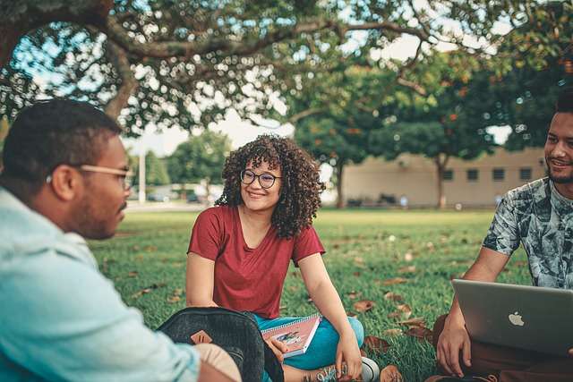 Groep studenten die samen in een park zitten, met een laptop en boeken, illustrerend het belang van samenwerking en gepersonaliseerd leren in het onderwijs.