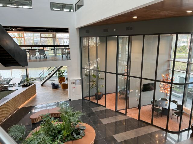 Moderne kantoorruimte van Stratlane Certification BV in Amsterdam, met uitzicht op het landschap, glazen wanden, planten, en een uitnodigende zithoek.