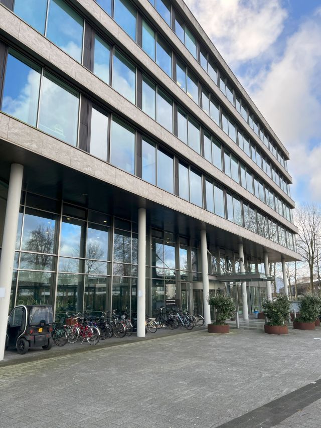 Kantoor van Stratlane Certification in Amsterdam met glazen gevel, fietsenstalling en entree, weerspiegeld in de ramen.