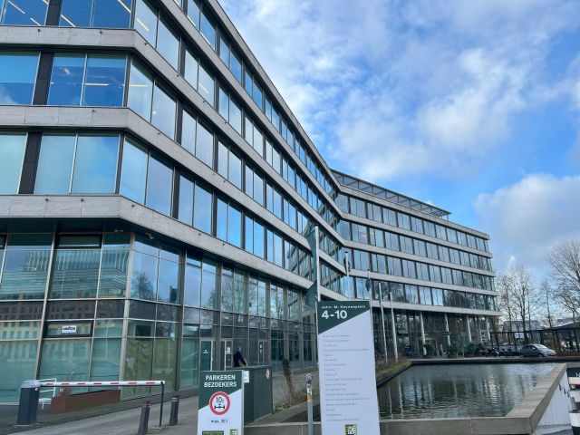 Moderne kantoorgebouw met glazen gevel en waterpartij, locatie voor ISO 21001 certificering en audits in Nederland.